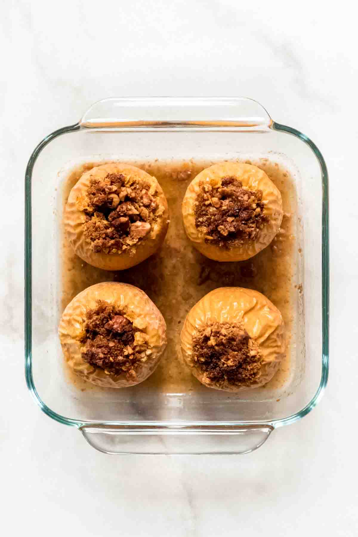 Four baked apples in a glass baking dish.