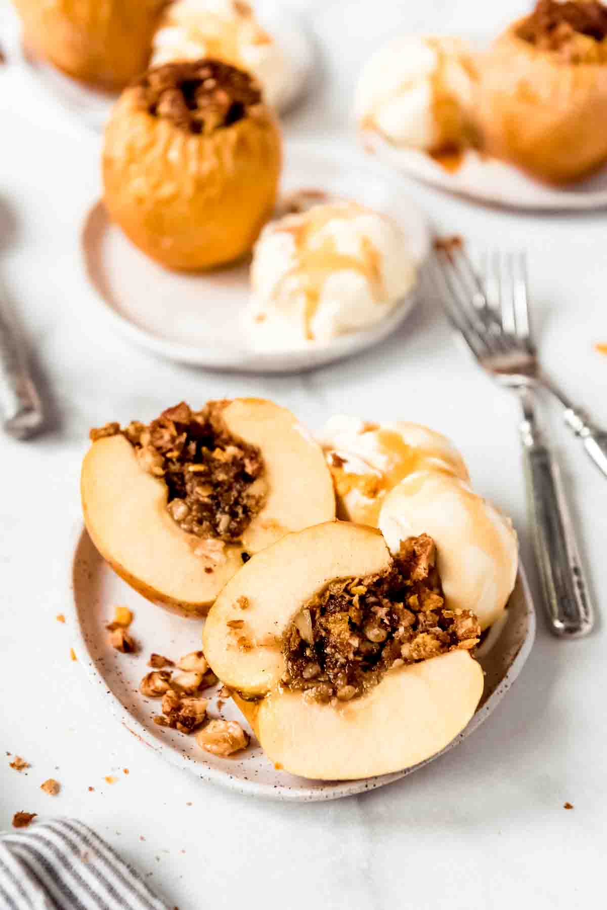 A baked apple that has been cut in half on a plate with ice cream, with more baked apples in the background.