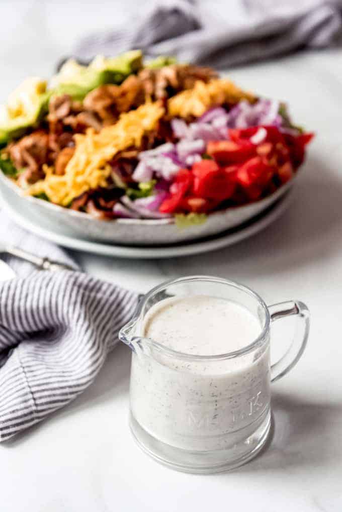 A glass pitcher of ranch dressing in front of a bbq chicken cobb salad.
