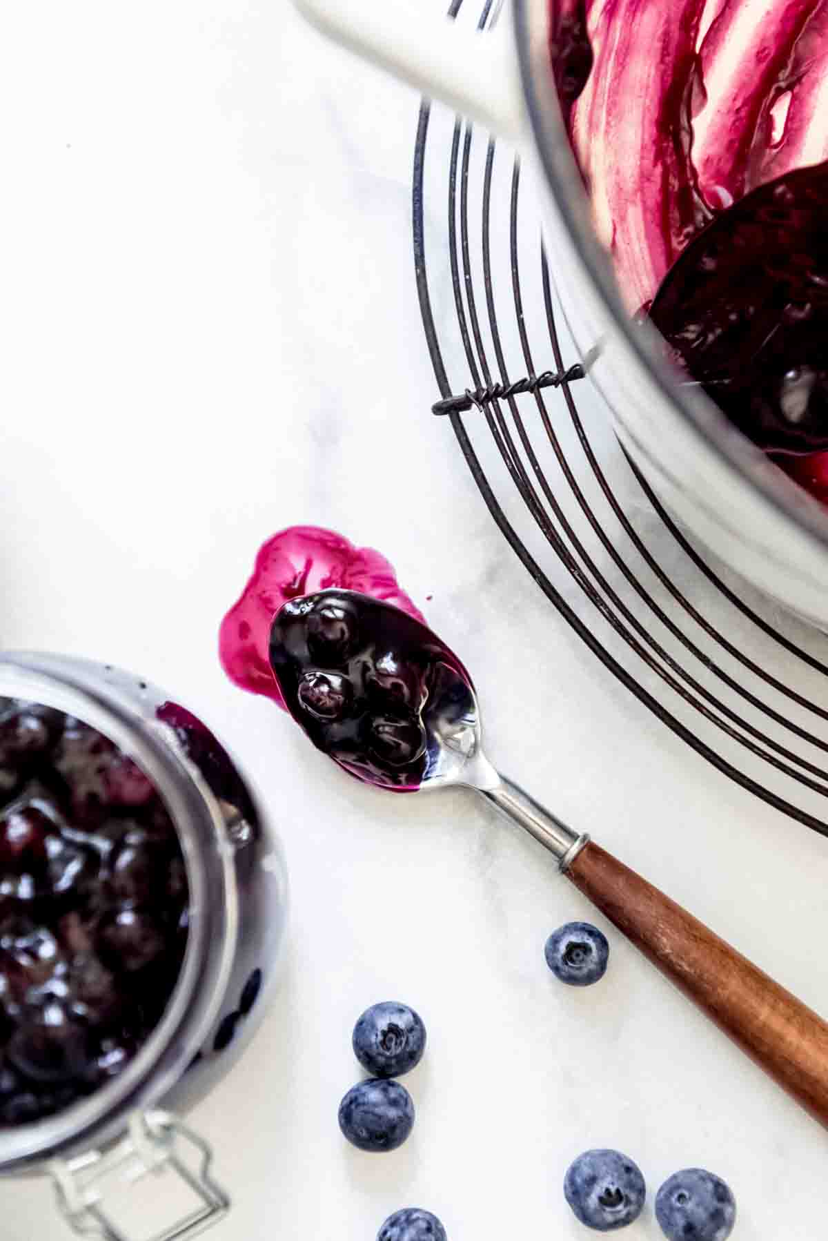 A spoonful of blueberry pie filling beside a pot of pie filling cooling on a wire rack.