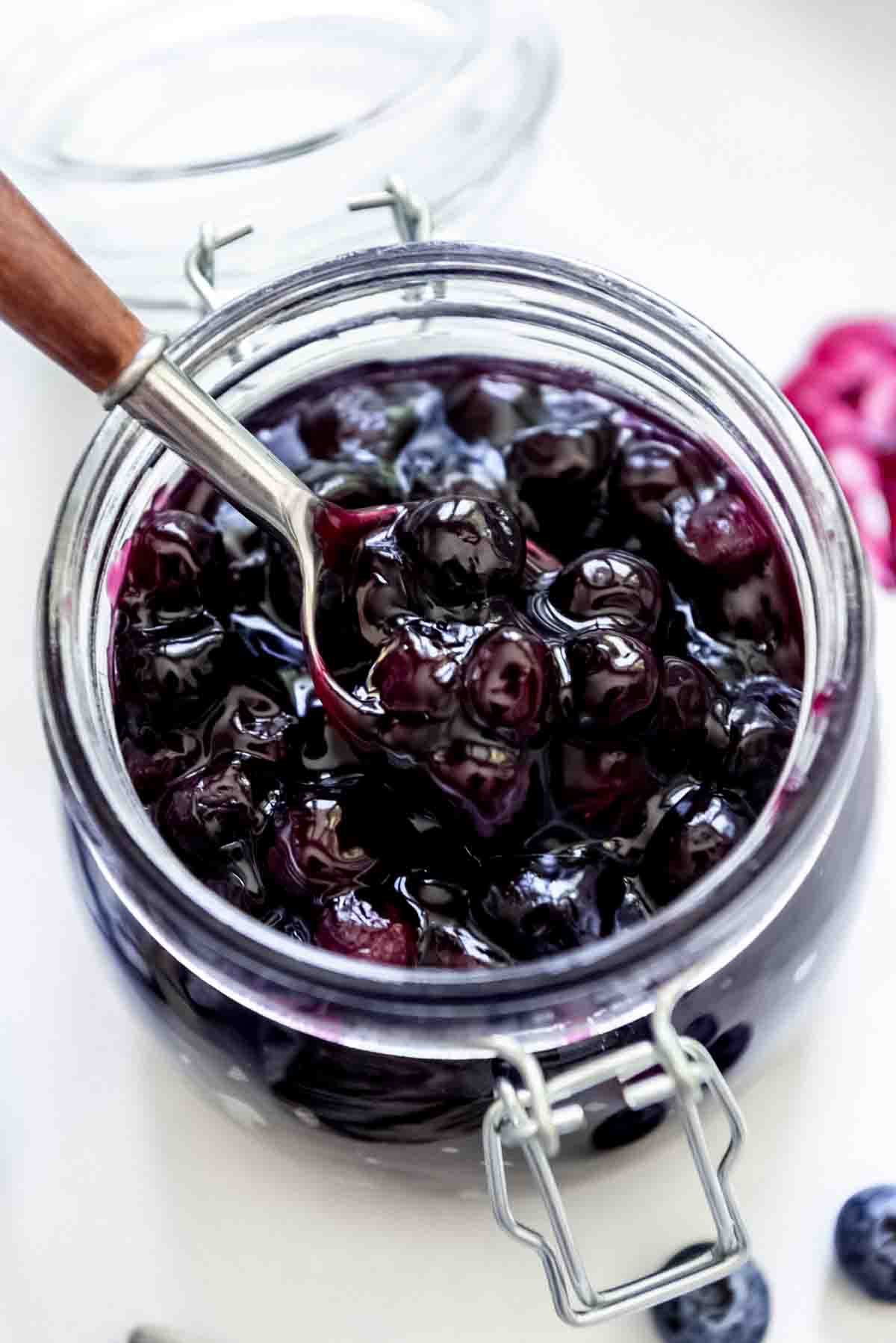 A glass jar of blueberry pie filling with a spoon lifting up some of the filling.