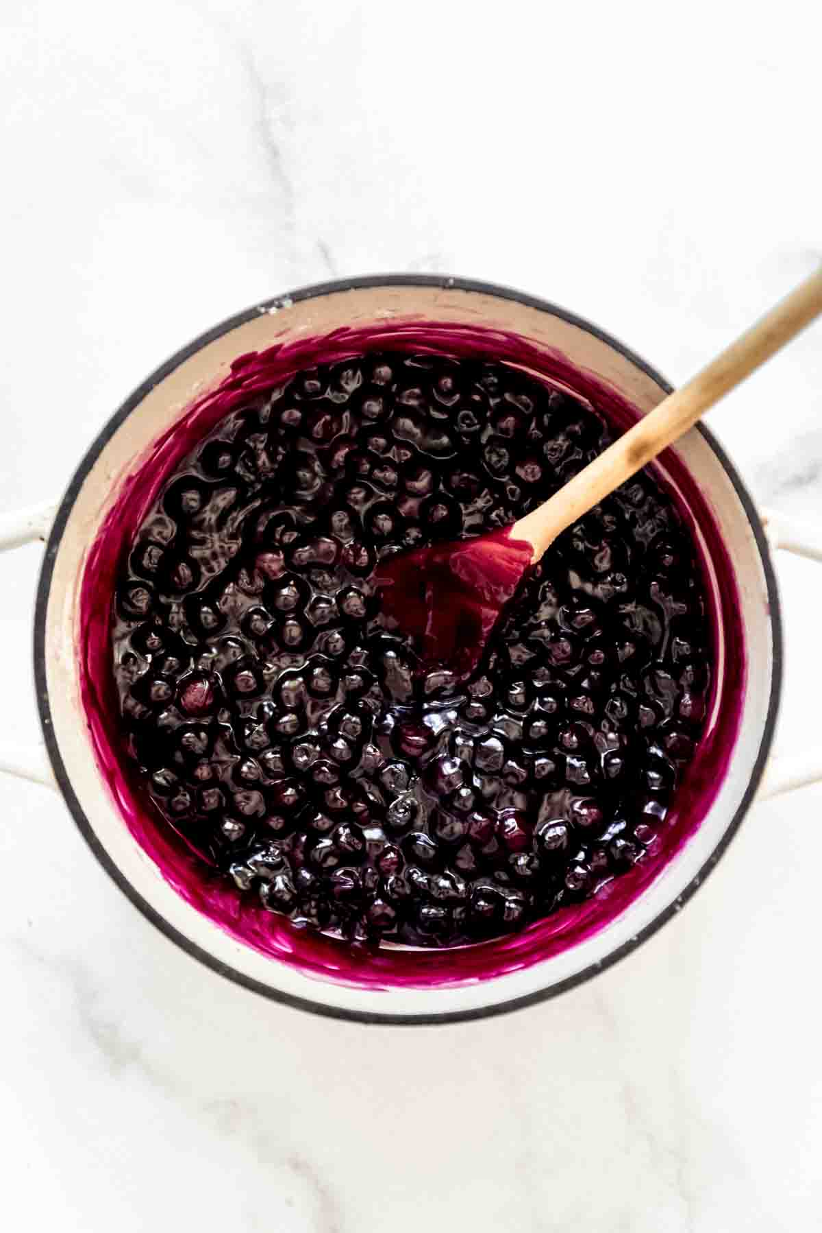 A large pot full of dark purple blueberry pie filling with a wooden spoon in it.