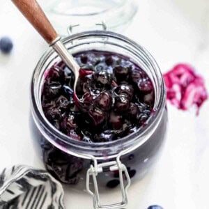 A glass jar of blueberry pie filling with a spoon lifting up some of the filling.