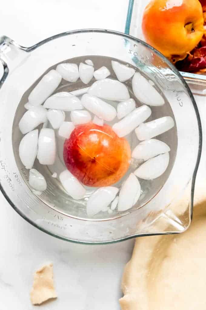 a scored peach in an ice bath