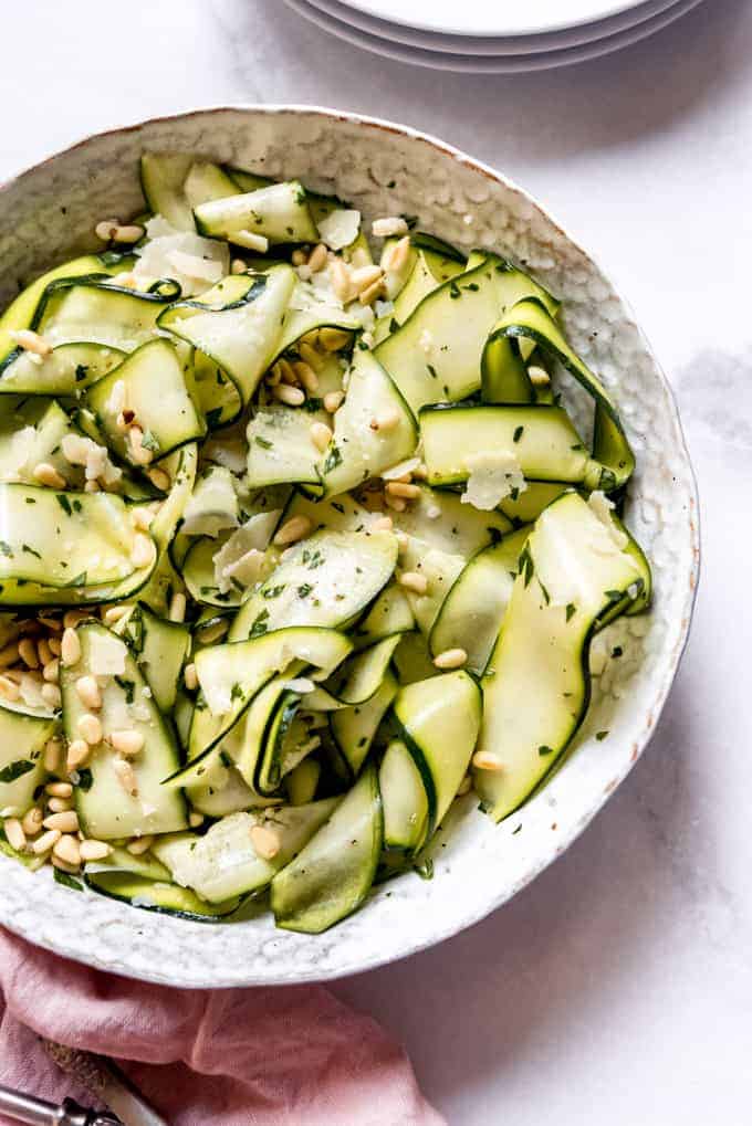 A serving bowl full of zucchini ribbon salad with pine nuts, herbs, and parmesan cheese sprinkled on top.