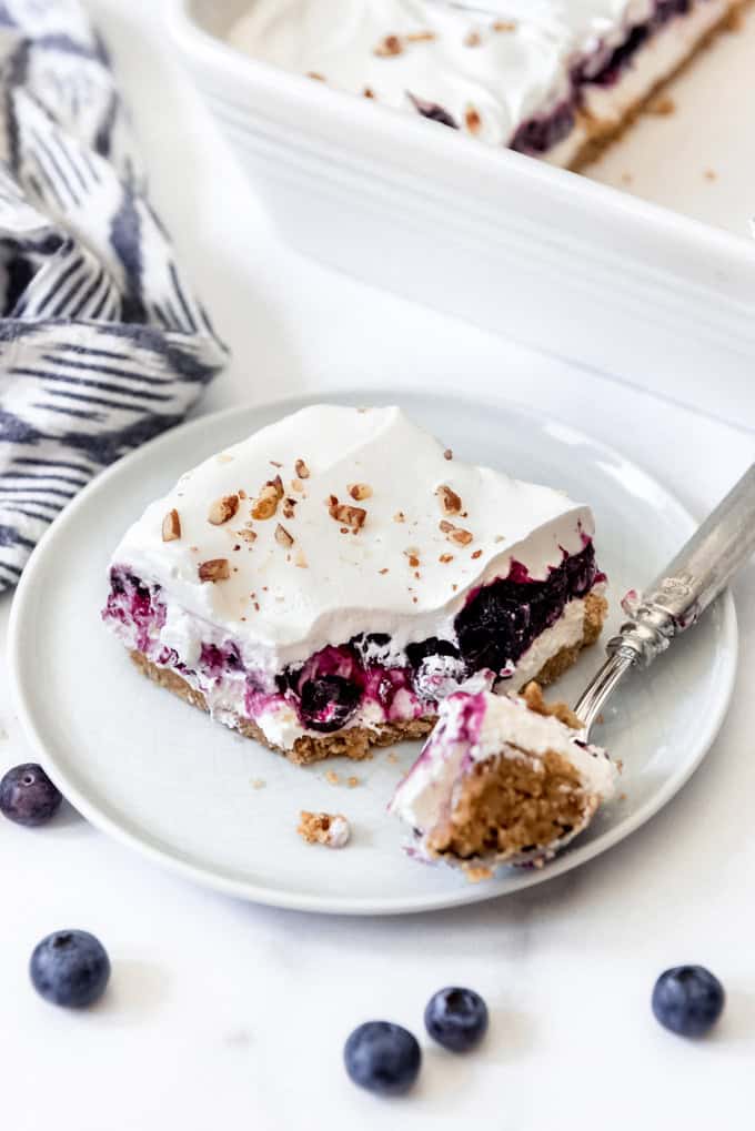 A slice of creamy blueberry delight dessert on a plate with a bite of it on a fork.