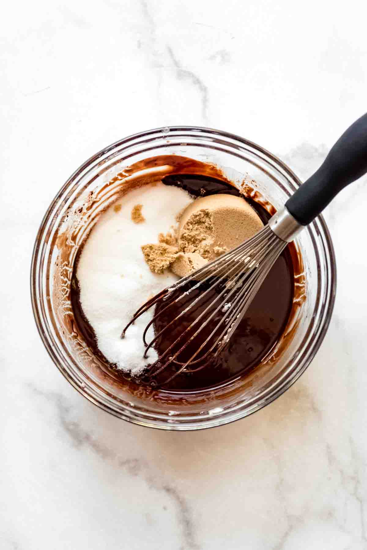 Adding vanilla and sugars to the melted chocolate and butter with a whisk.