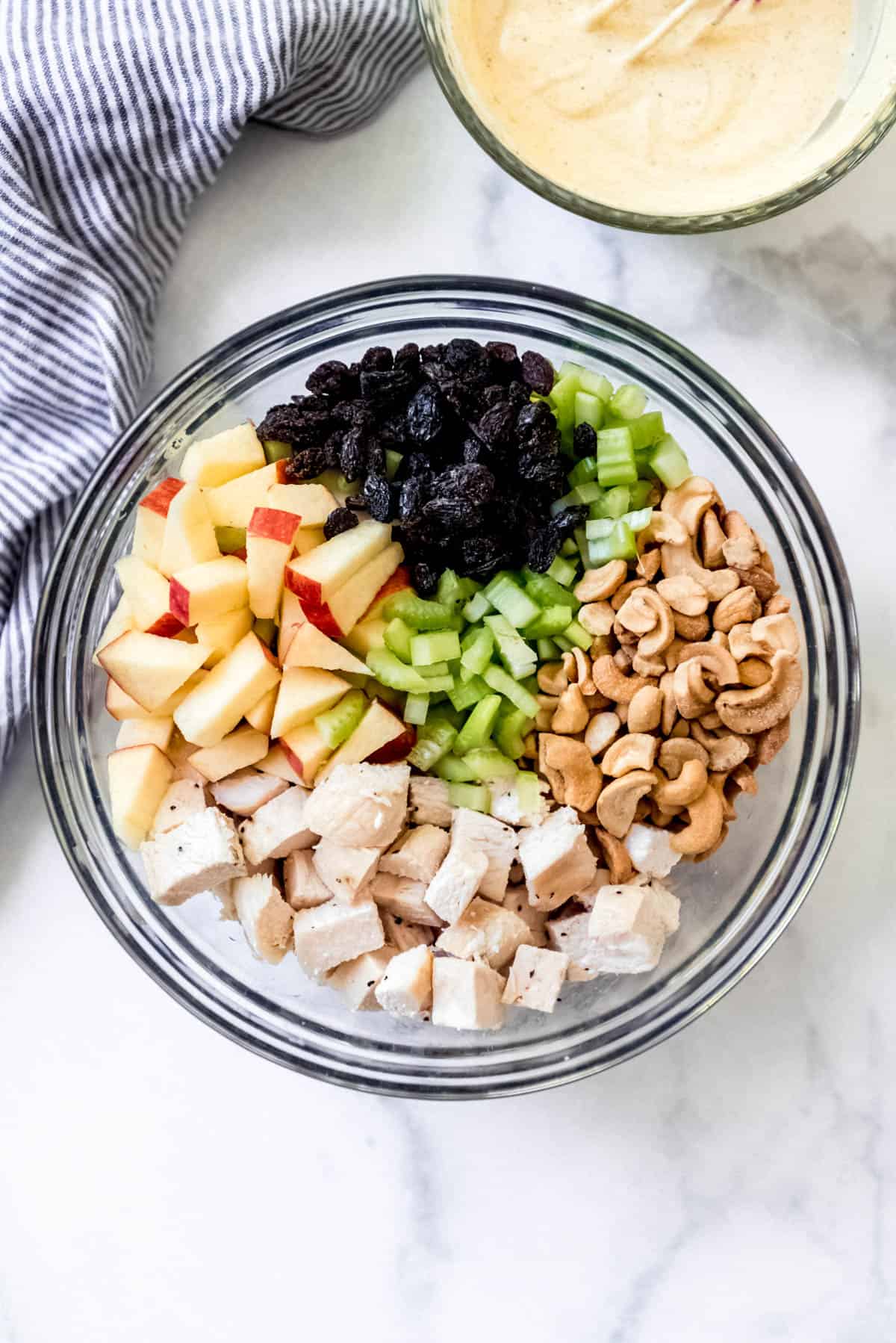 Chicken chunks, cashews, celery, raisins, and chopped apples in a glass bowl.