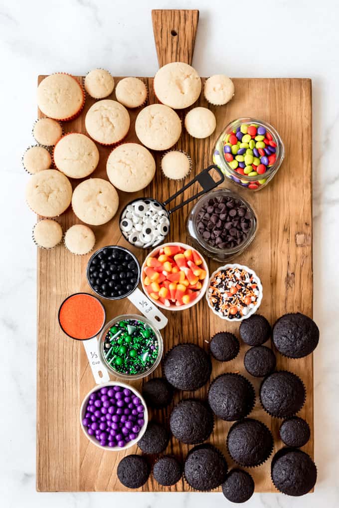A board with cupcakes and bowls of sprinkles and candy on it.