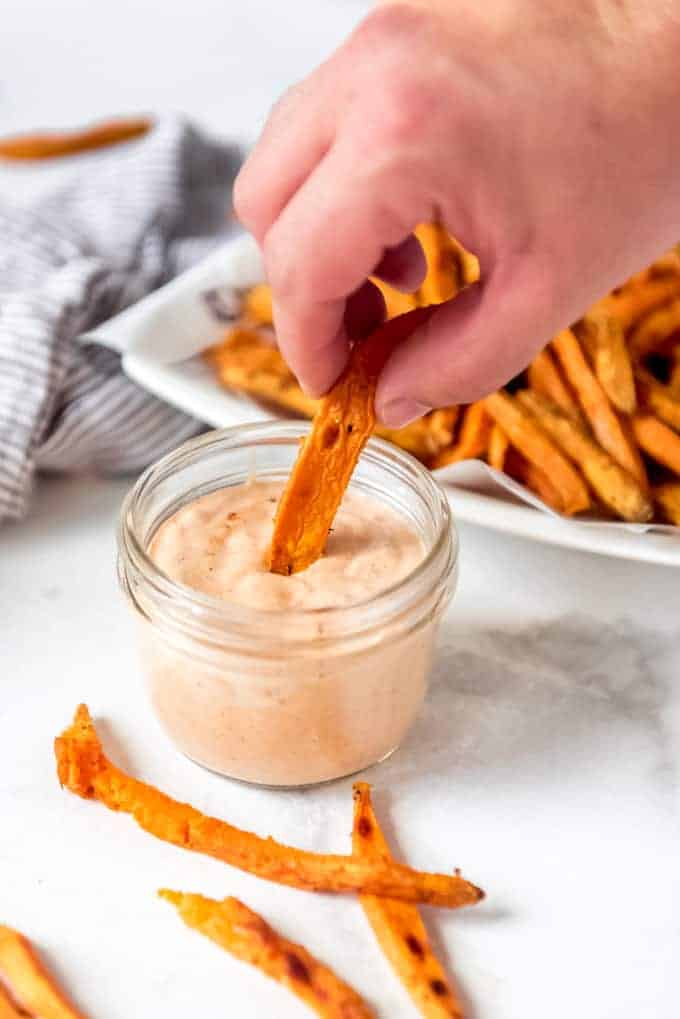 A hand dipping a sweet potato fry into a dipping sauce.