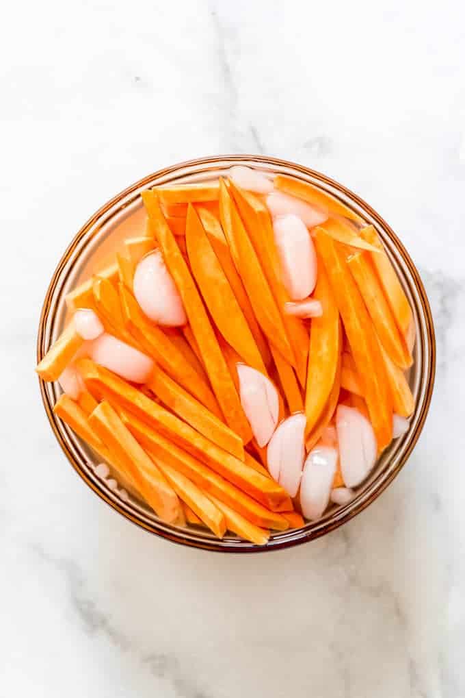 a bowl of sliced sweet potato fries in a bowl of ice water