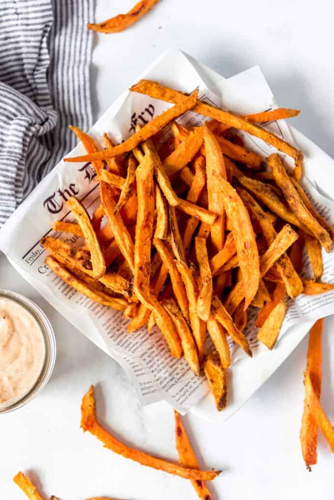 Sweet potato fries piled on a plate lined with newsprint parchment paper.