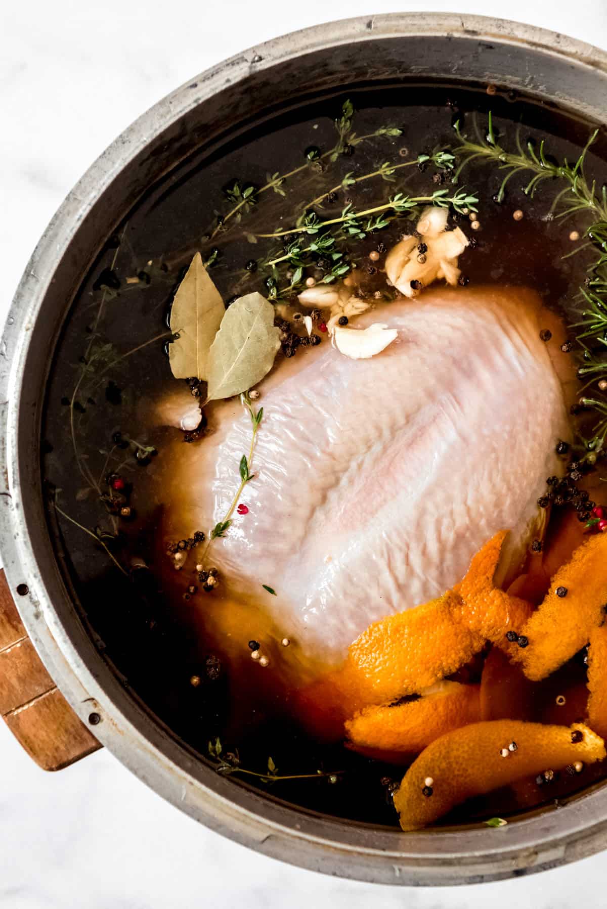 A turkey soaking in brine with herbs, orange peel, and peppercorns.