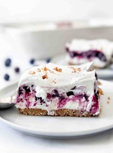 A slice of blueberry delight topped with whipped cream and pecans on a plate.