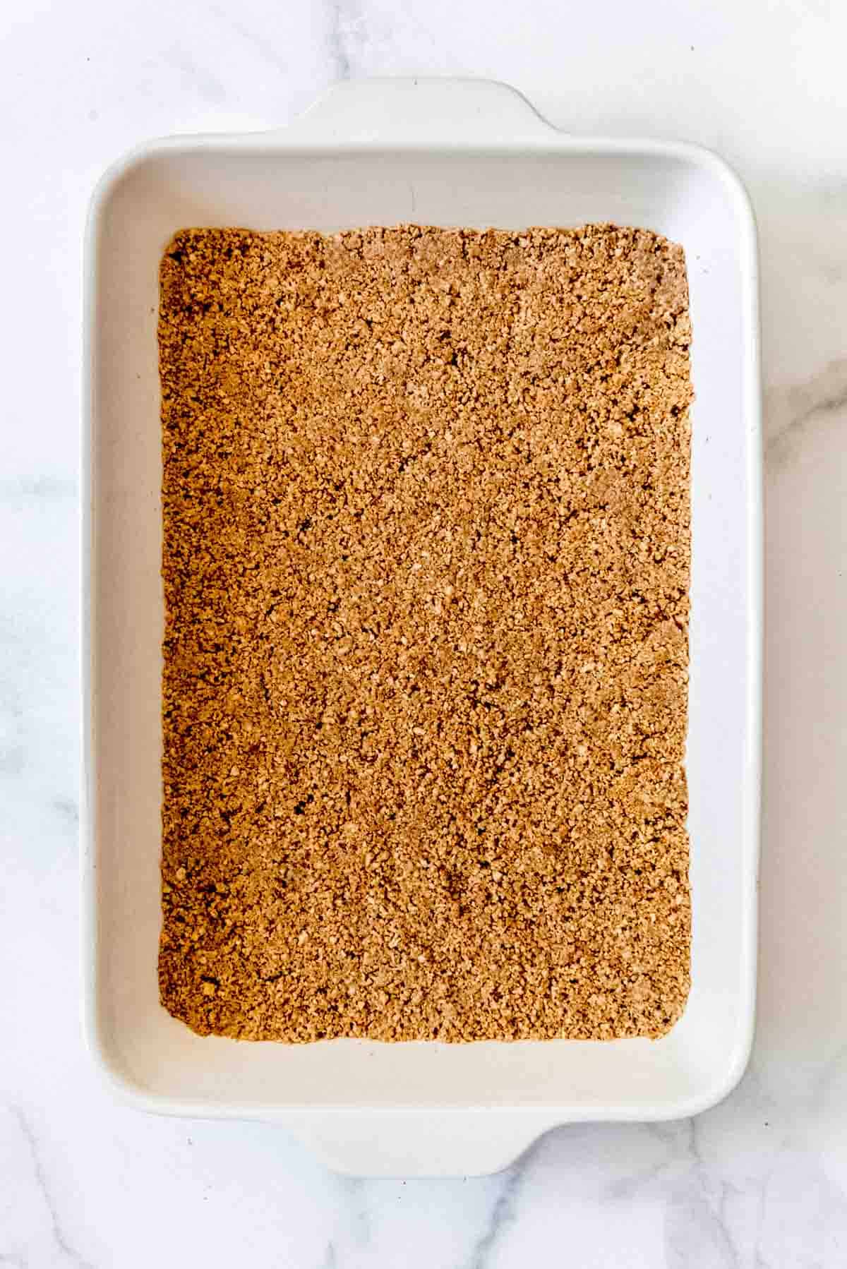 pressed graham cracker and pecan crust in the bottom of a large white baking pan