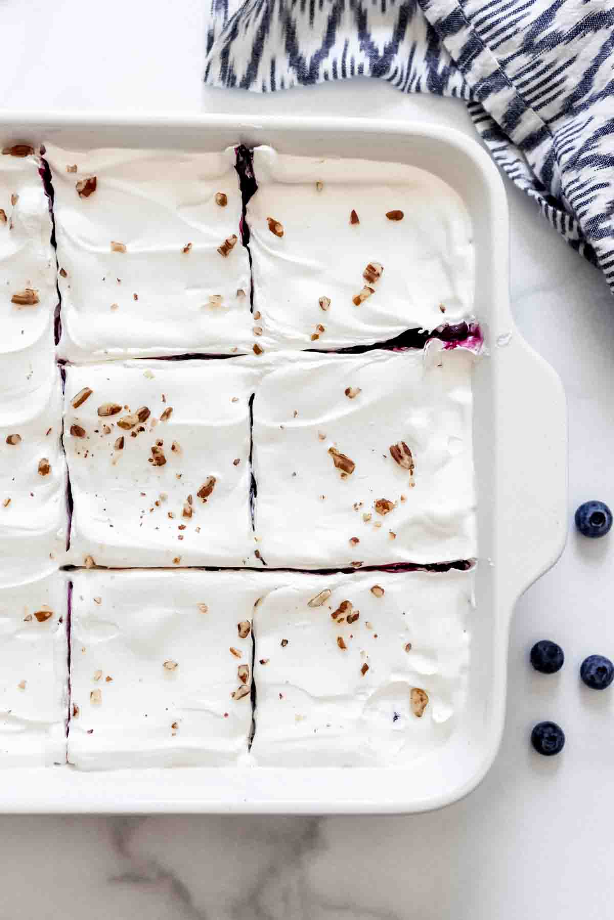 Sliced squares of blueberry delight dessert in a white baking dish.