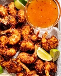 Coconut shrimp on a baking sheet with sweet chili dipping sauce in a bowl next to them.