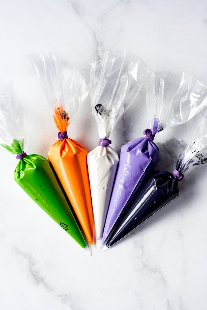 Bags of royal icing in green, orange, white, purple, and black. 