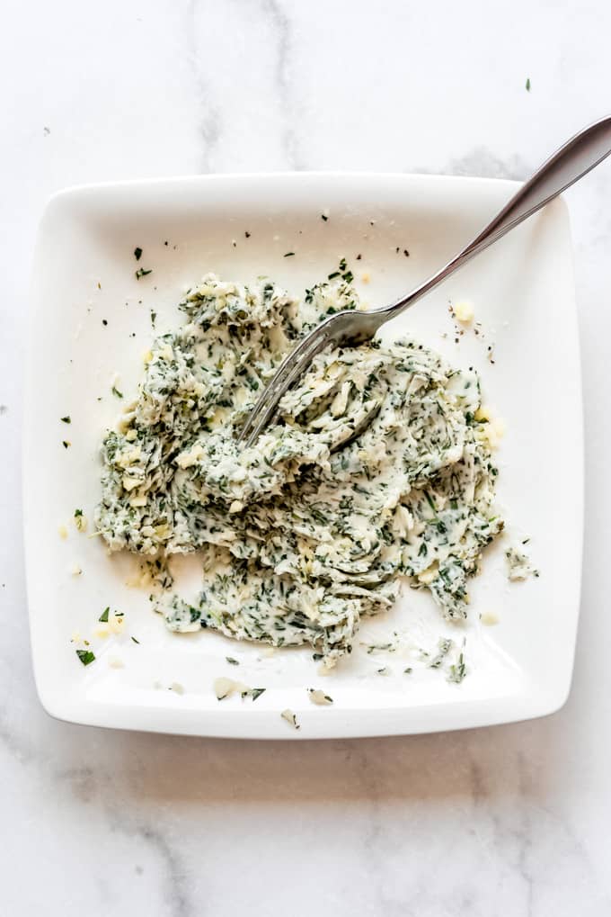 Mashed garlic herb butter on a white plate with a fork.