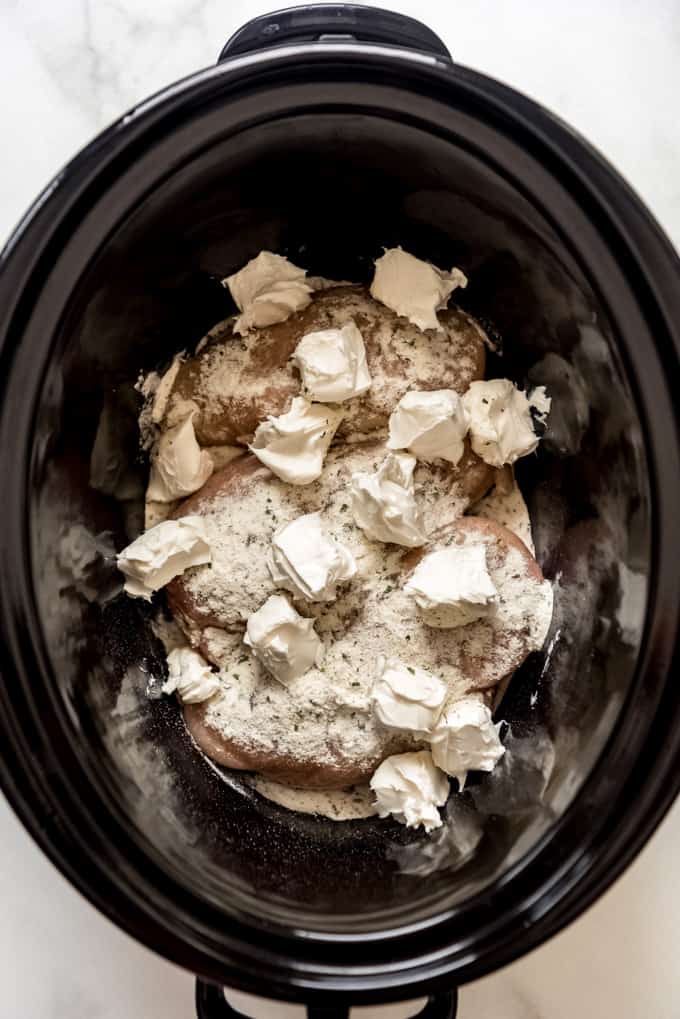 Chicken sprinkled with powdered ranch dressing and cubes of cream cheese in a crock pot.
