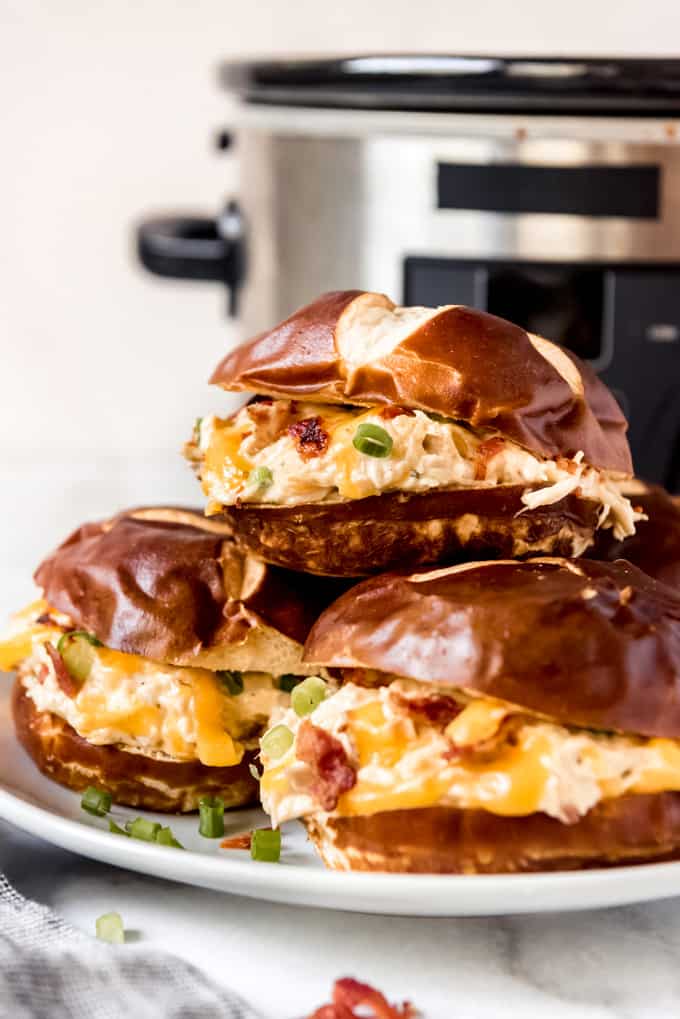 Three crack chicken sandwiches on pretzel buns stacked on a plate.