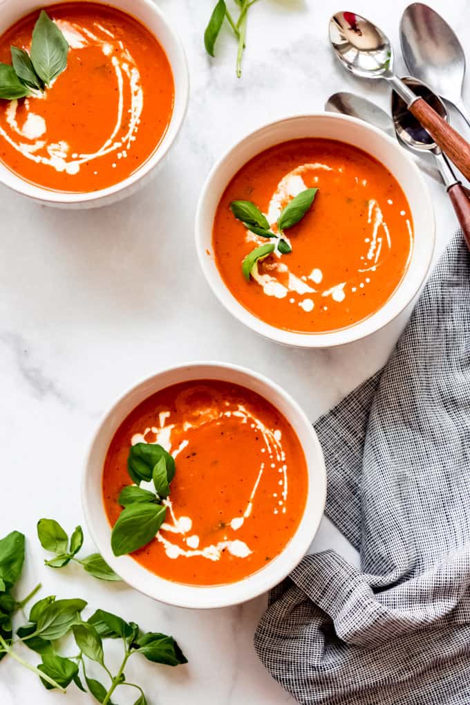 overhead shot of 3 tomato basil soup bowls drizzled with cream, garnished with fresh basil