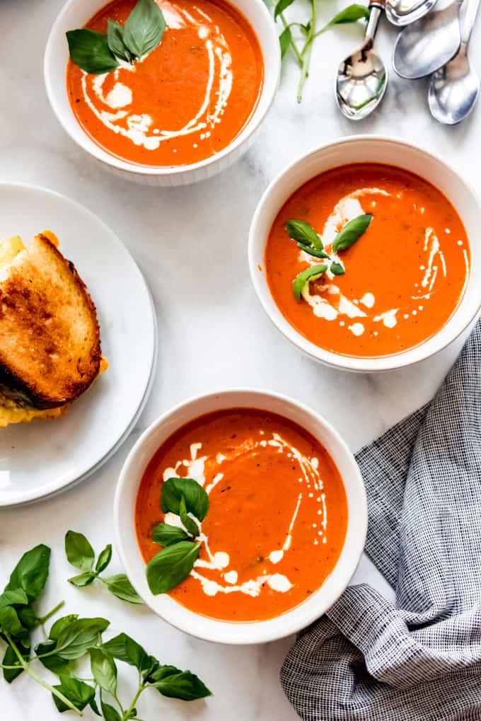 Over head shot of 3 tomato soup bowls drizzled with cream, with fresh basil and grilled cheese