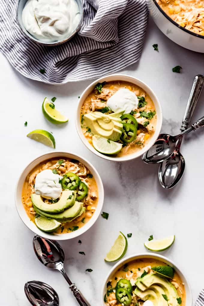 Homemade chicken chili garnished with lime wedges, avocado, jalapenos, and sour cream.