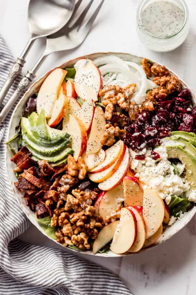 A large salad bowl with lettuce, bacon, apples, avocados, and walnuts.
