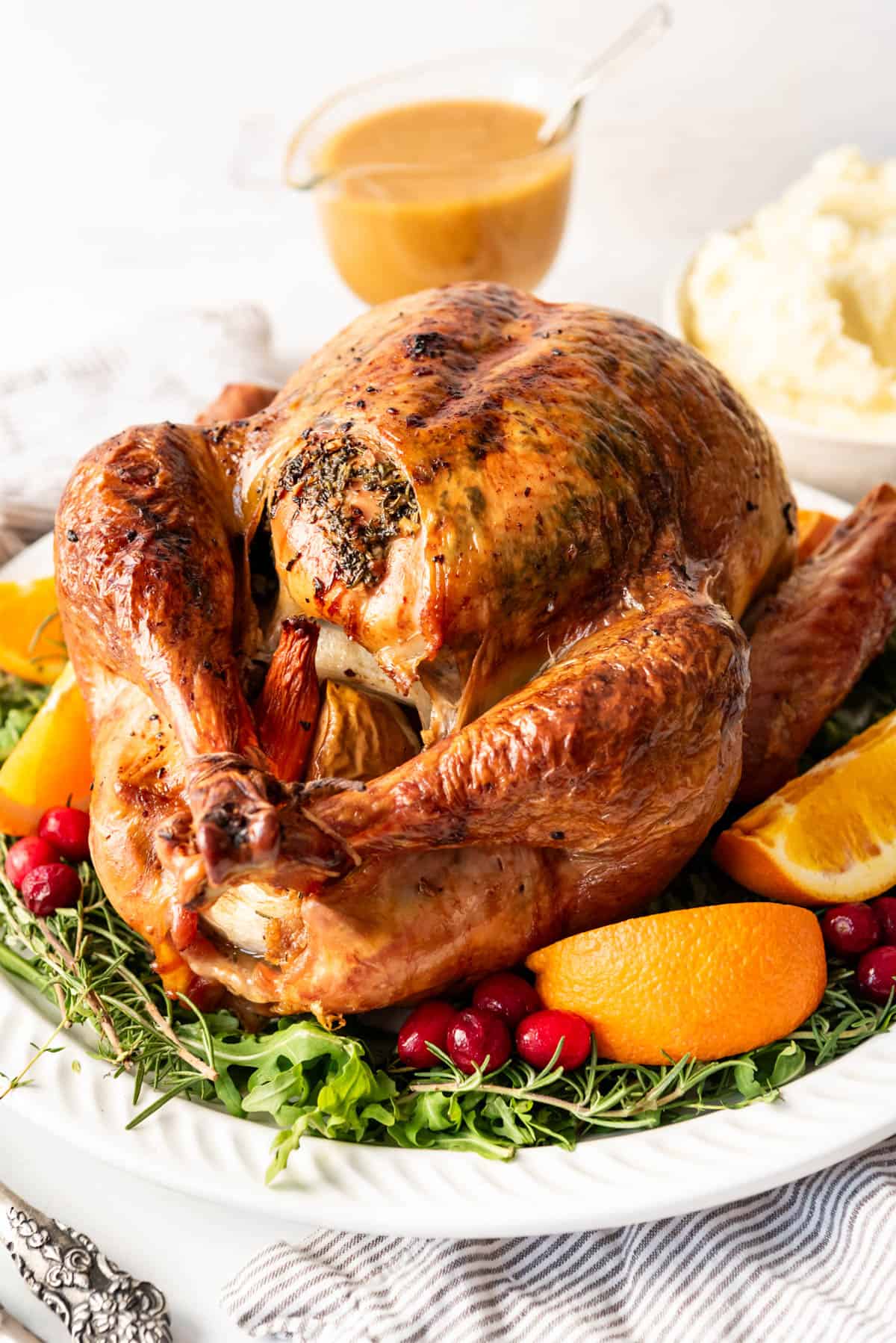 A roast Thanksgiving turkey on a platter garnished with fruit and herbs.