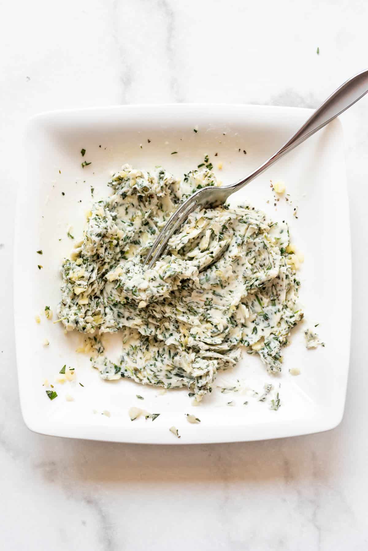 Mashed garlic herb butter on a white plate with a fork.