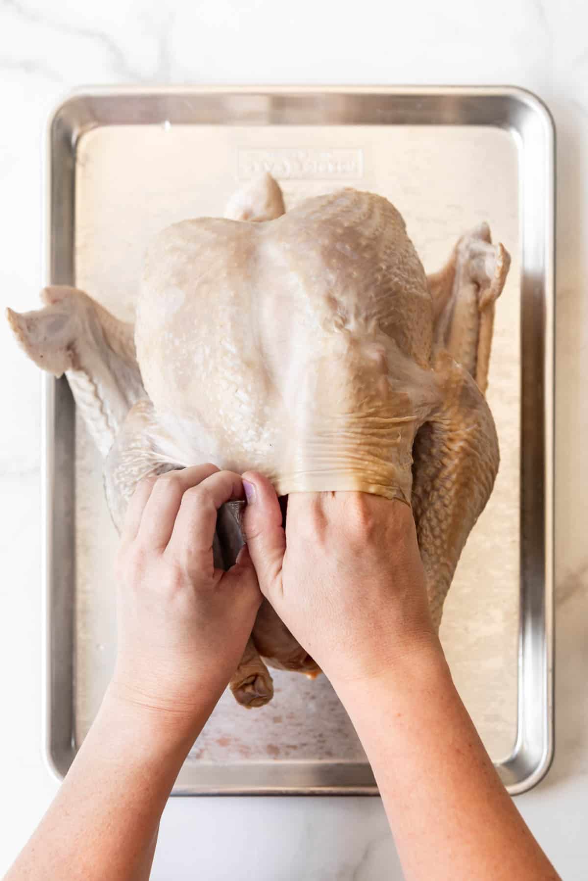 A hand loosening the skin of a turkey on a baking sheet.