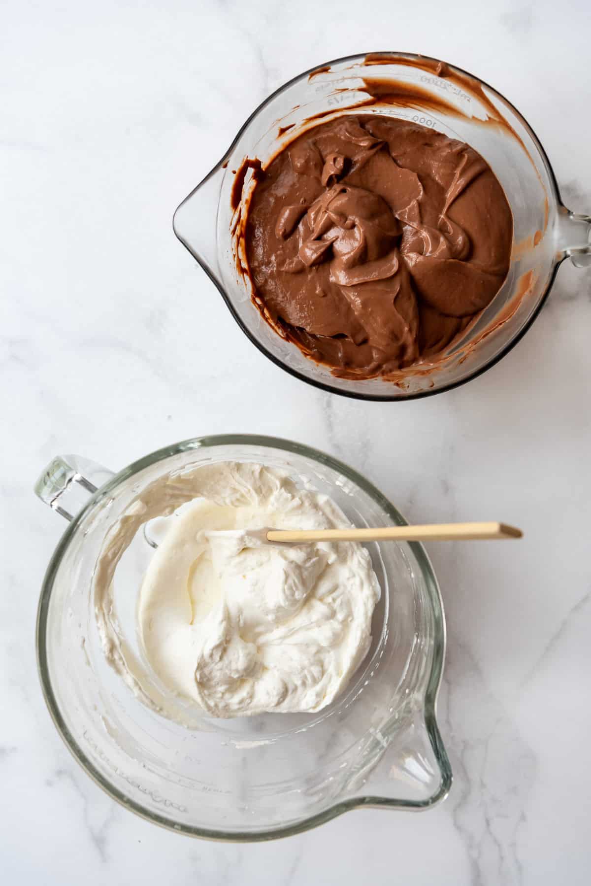 An overhead image of a bowl of whipped cream and a bowl of chocolate pudding.