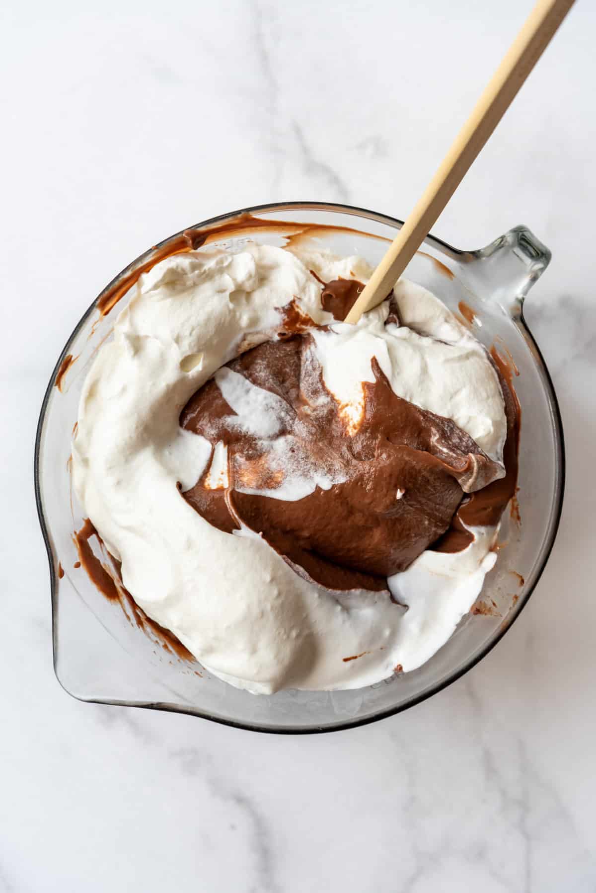 An overhead image of whipped cream being folded in to a bowl of chocolate pudding.