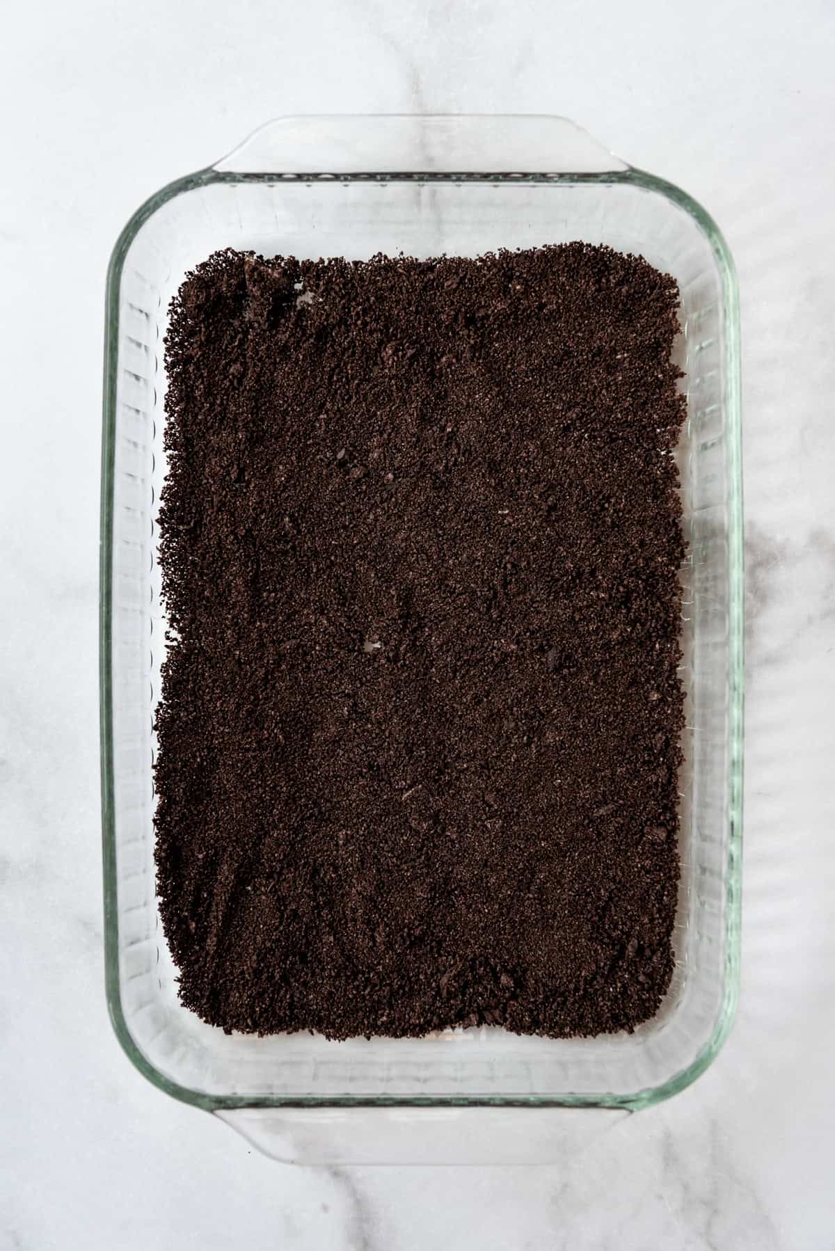 An overhead image of a layer of graham cracker crumbs in a 9x13-inch glass baking dish.