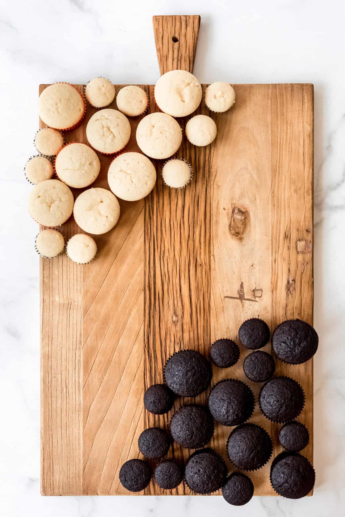 A large board with unfrosted white and chocolate cupcakes on it.