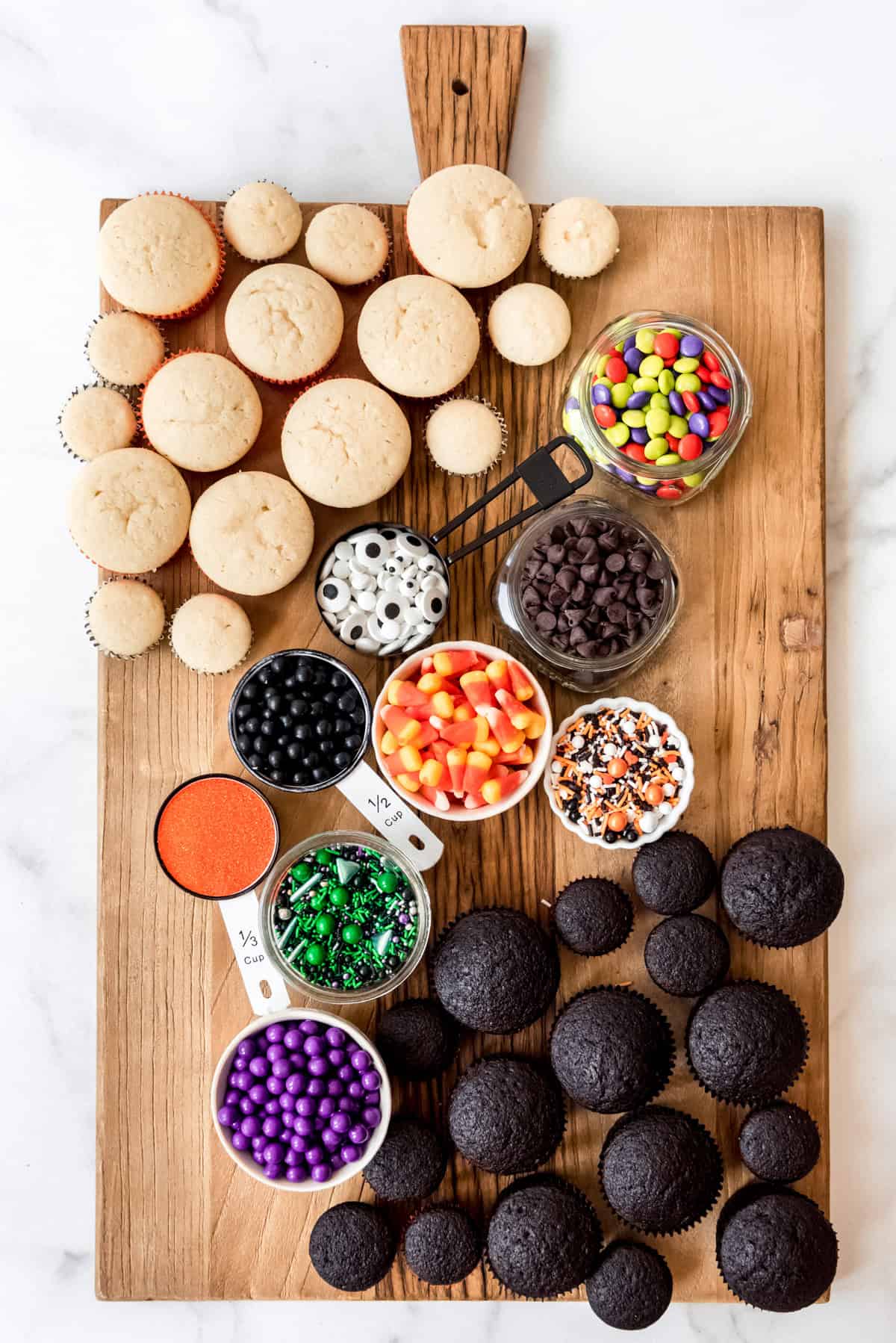 A board with cupcakes and bowls of sprinkles and candy on it.