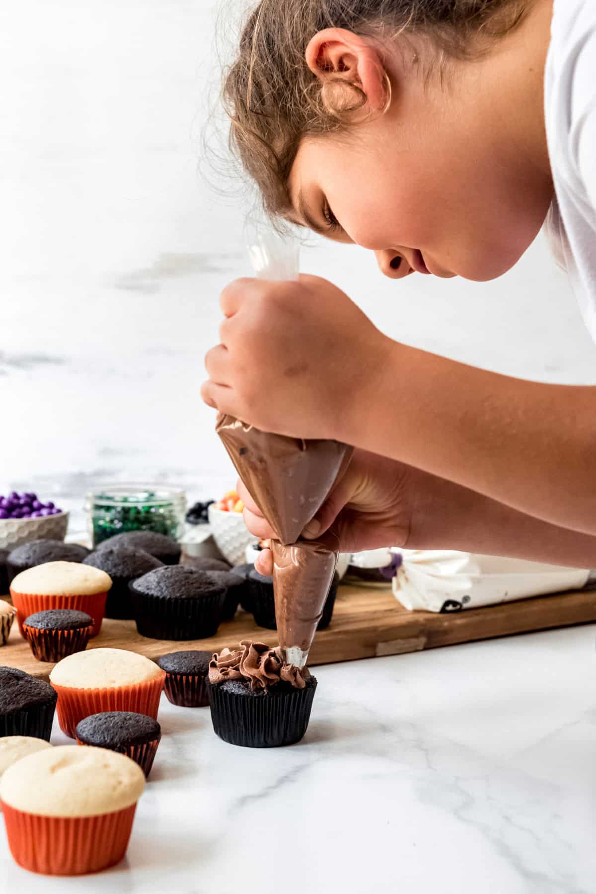 A child piping chocolate frosting onto a cupcake.