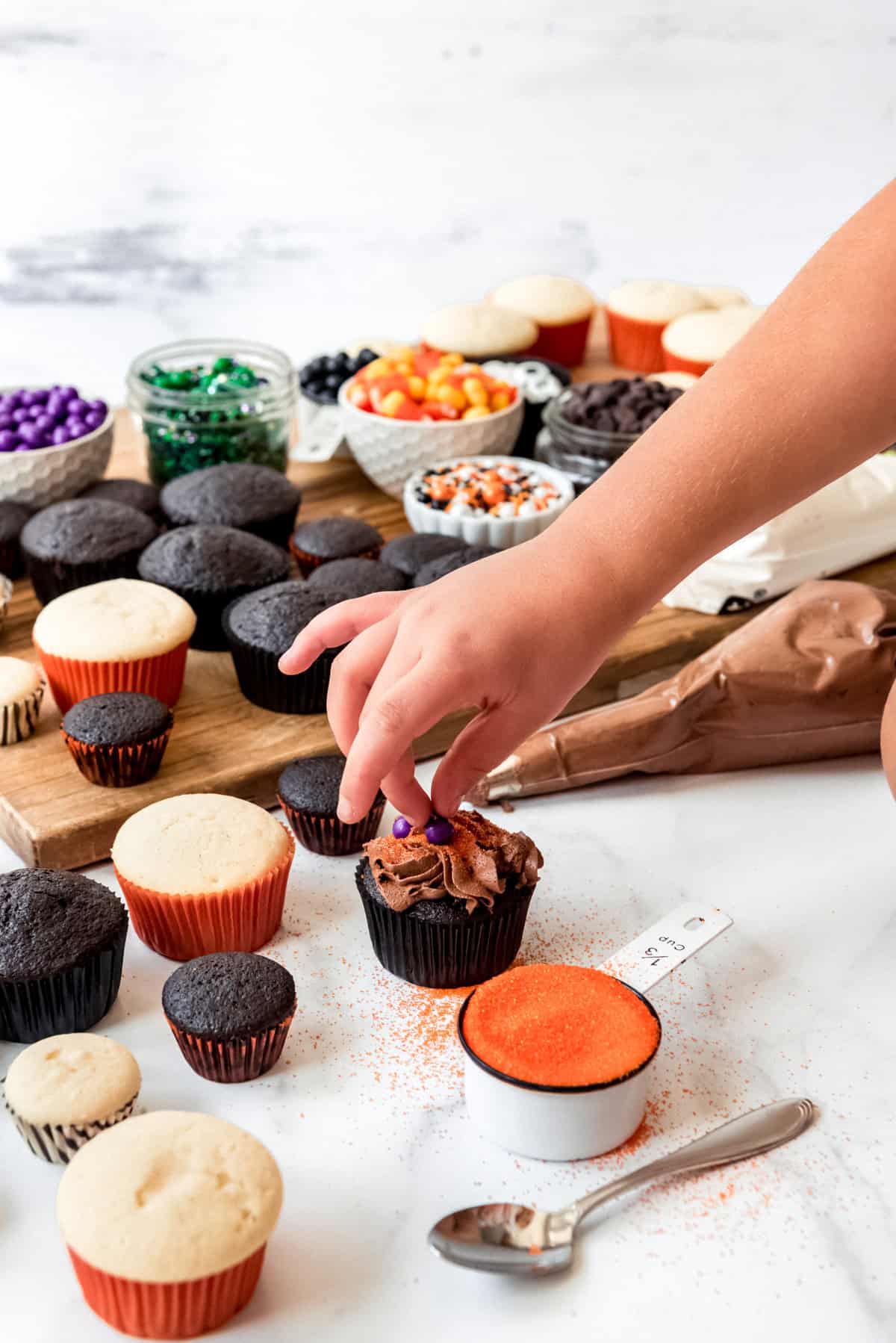 A child's hand placing candy sprinkles and decorations on a chocolate cupcake.