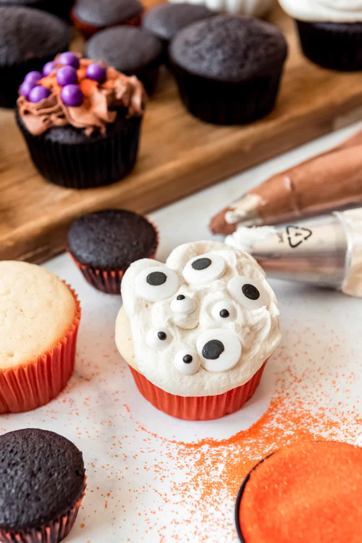 A white cupcake with vanilla frosting and googly eye candies on top.