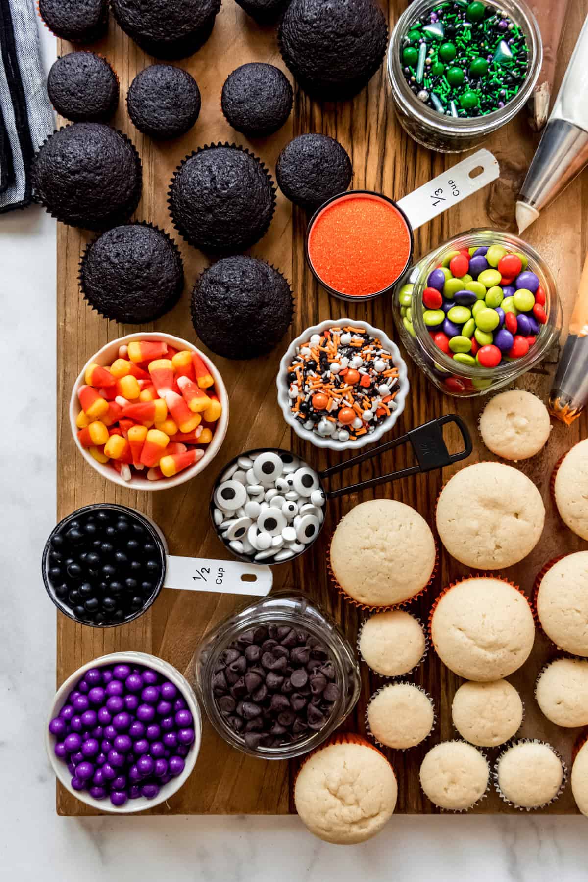 Halloween candy and sprinkles on a board with cupcakes ready for decorating.