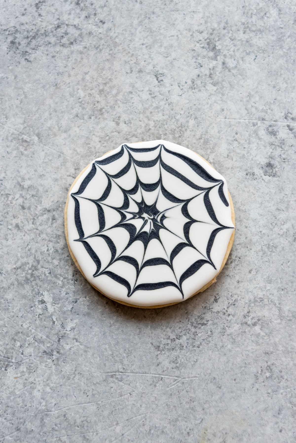 A sugar cookie decorated with icing to look like a spiders web.