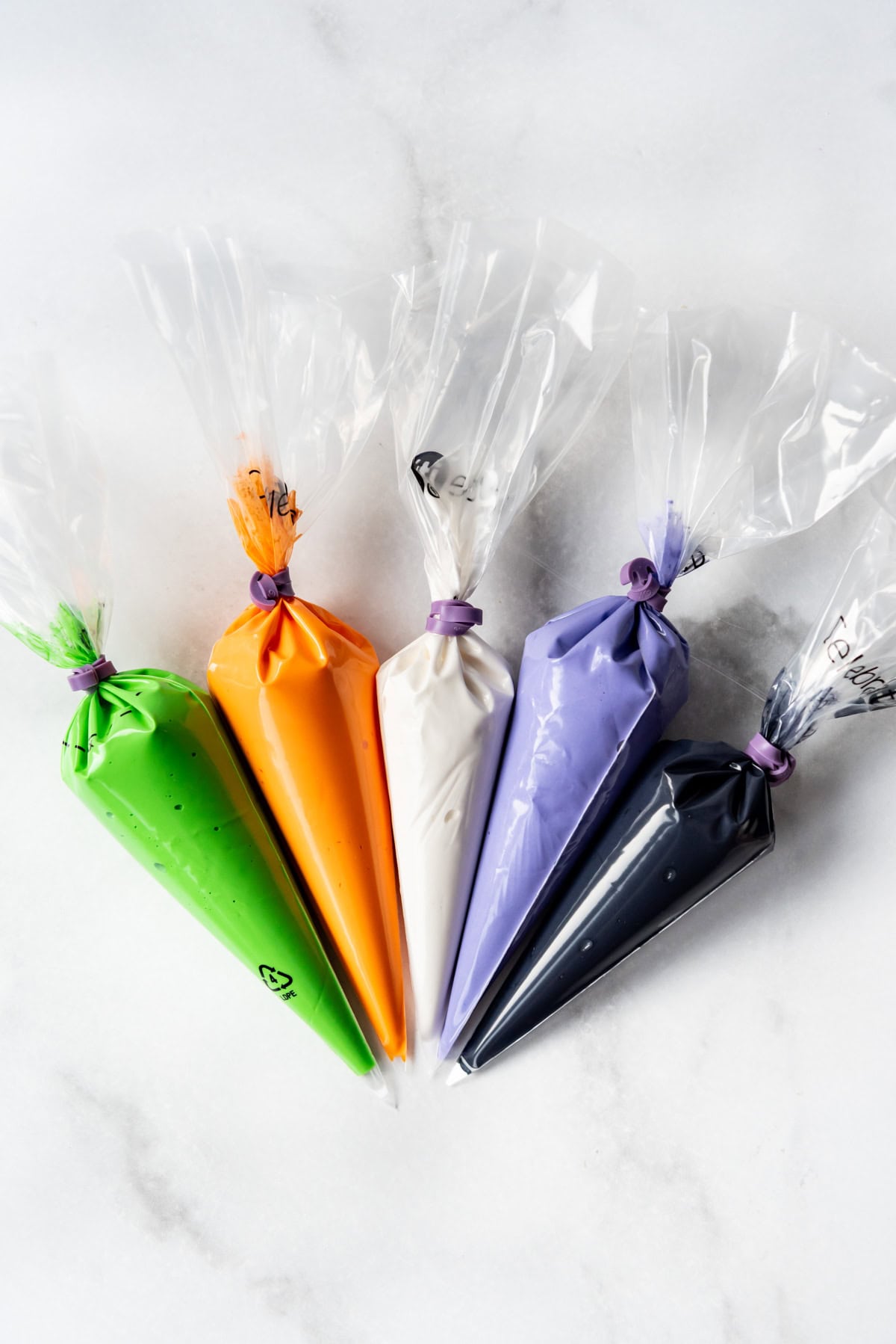 Bags of royal icing in green, orange, white, purple, and black. 