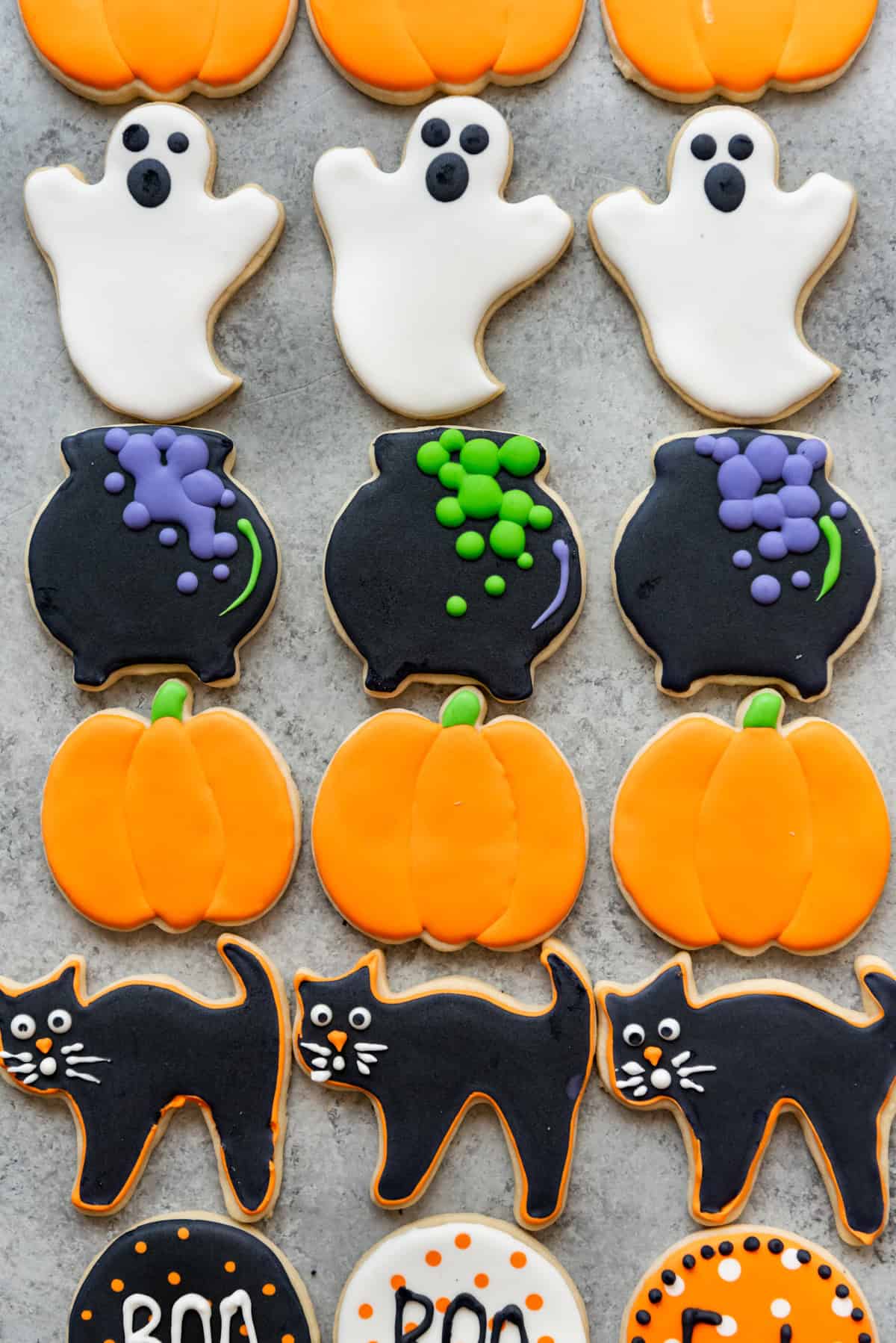 Rows of Halloween sugar cookies decorated like ghosts, cauldrons, pumpkins, and black cats.