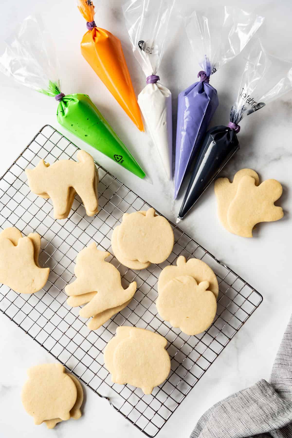 Undecorated sugar cookies next to bags of royal icing in Halloween colors.