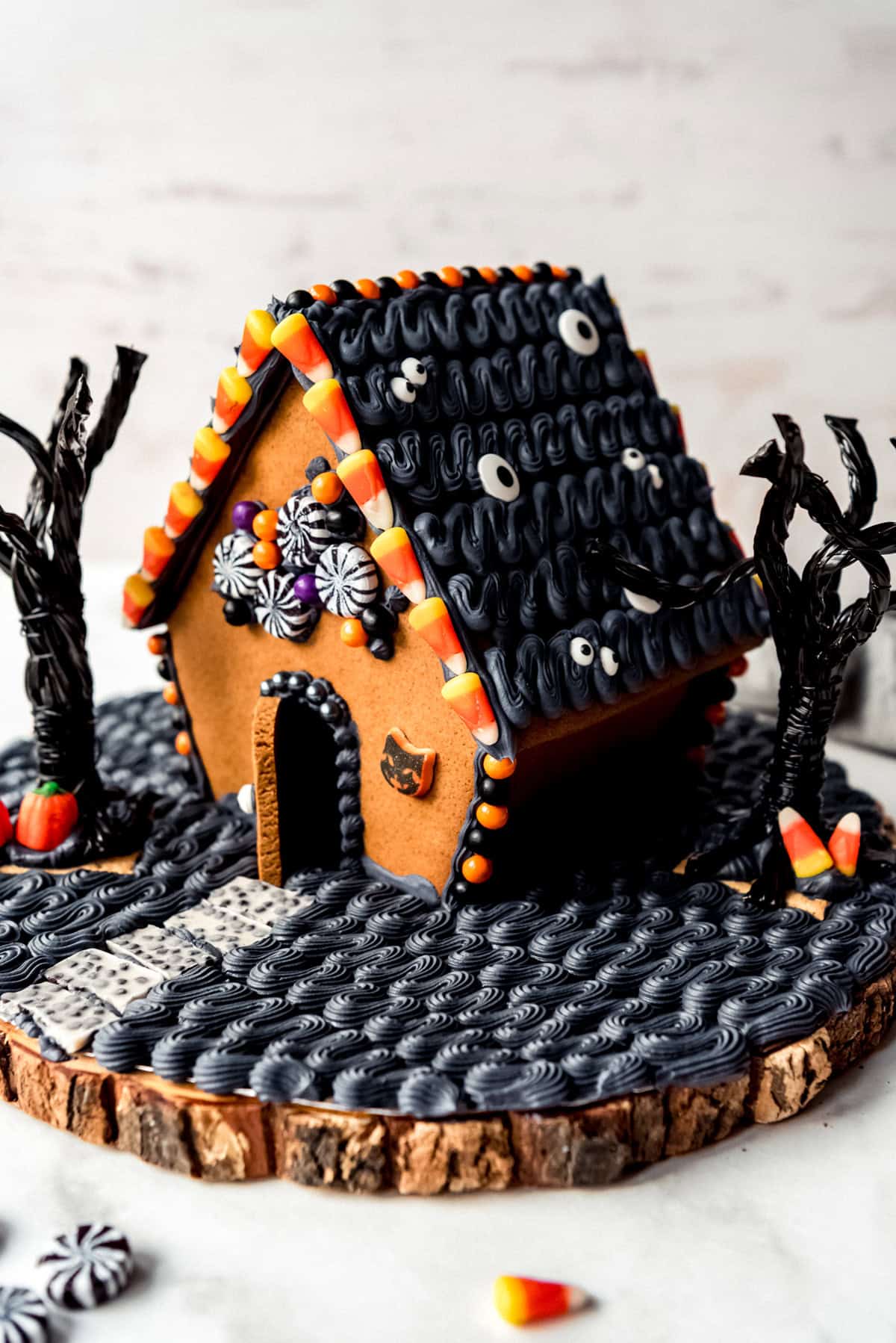 A gingerbread house decorated with black royal icing, candy, and licorice trees.