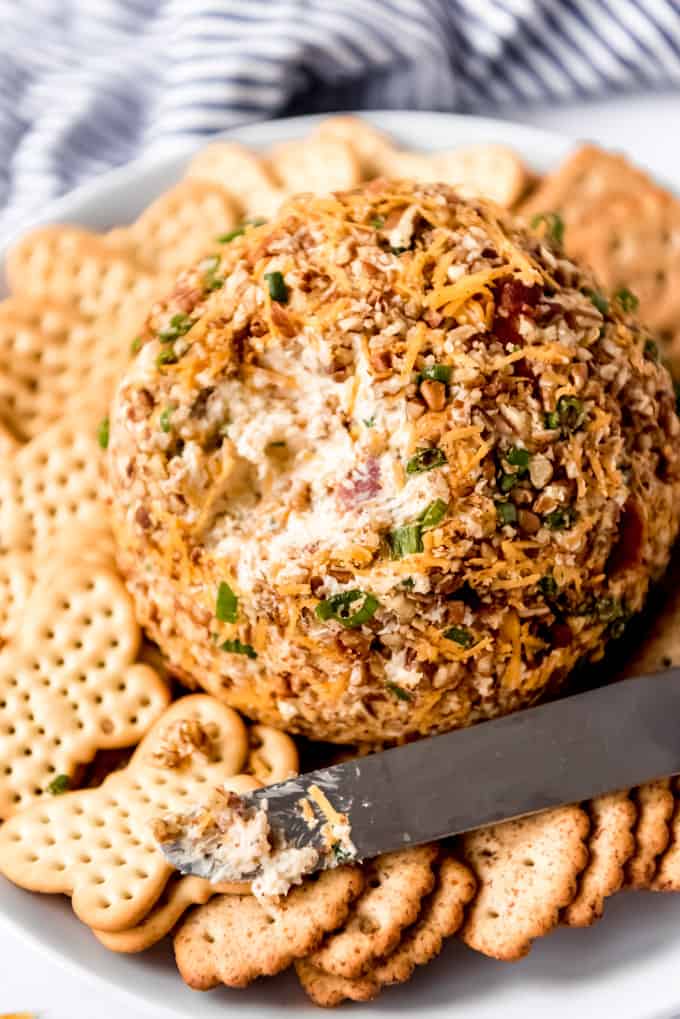 A cheese ball on a plate with crackers and a knife.