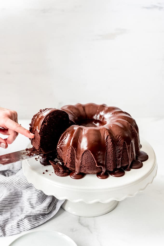 taking a slice of chocolate bundt cake on a cake stand