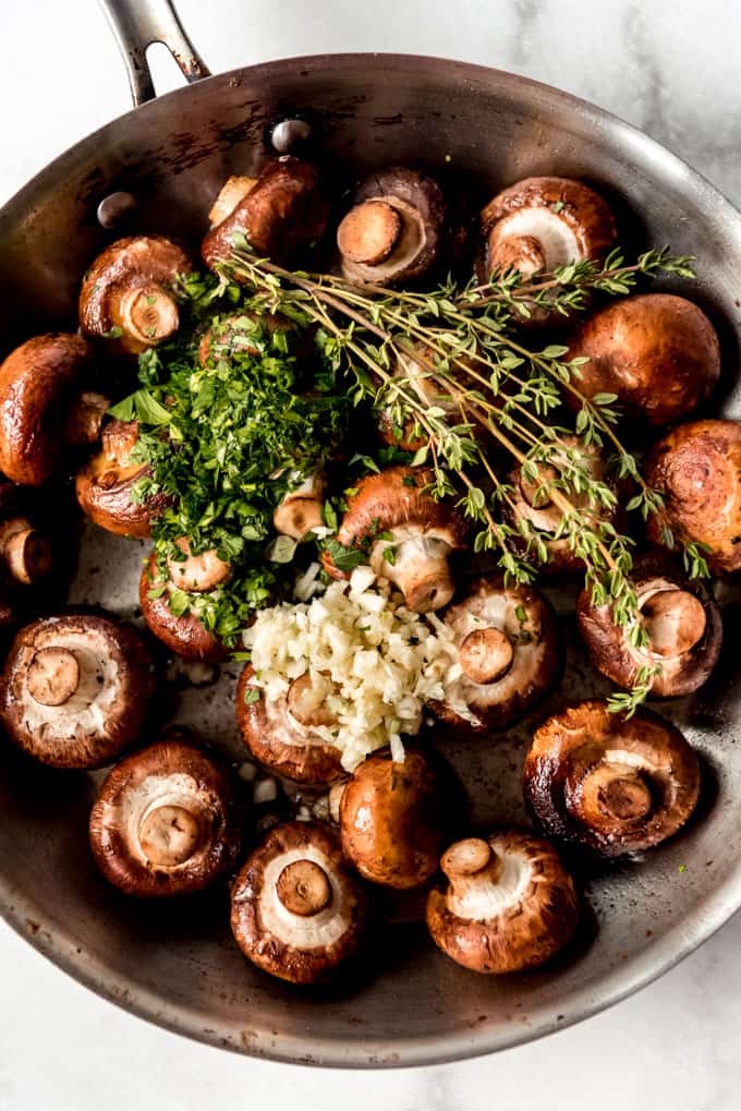 Mushrooms in a pan with minced garlic and fresh herbs.