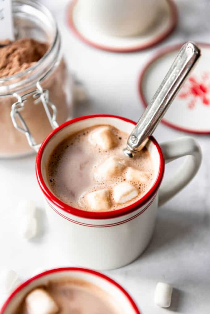 A mug of creamy hot chocolate with a spoon in it and marshmallows on top.